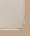 Close-up of the corner of an Outdoor Vista Sofa Cushion in beige, with a slightly darker beige border, set on a solid light brown surface.