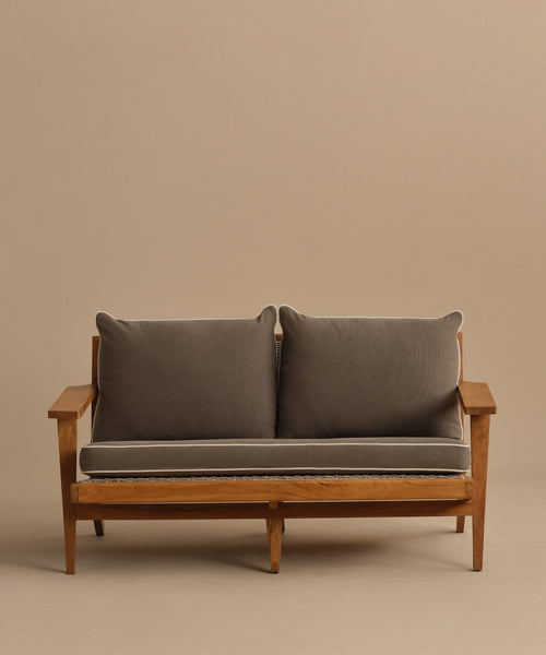The Outdoor Vista Sofa Cushion, featuring thick dark gray Italian fabric with light piping and a minimalist wooden frame, stands out against a plain beige background for a modern look.