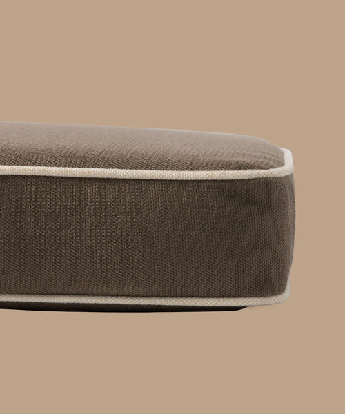 A close-up side view of the Outdoor Vista Sofa Cushion, a brown rectangular cushion with beige piping, made from Italian fabric and set against a plain beige background.