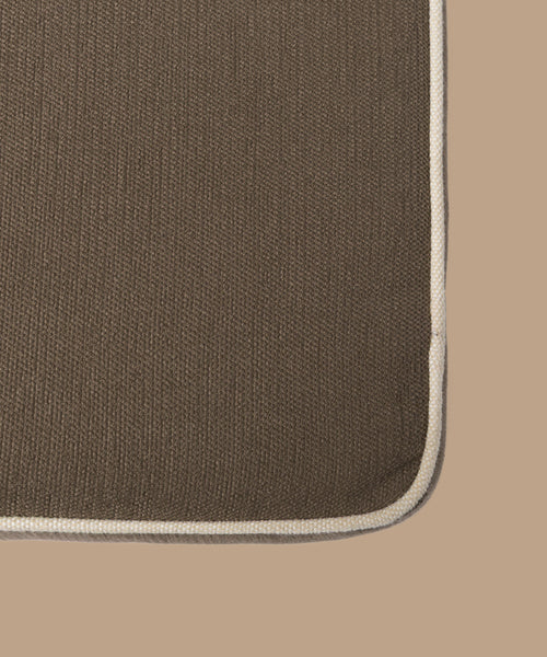 Close-up of the corner of the Outdoor Vista Sofa Cushion, a rectangular brown textured cushion with light beige trim, crafted from premium Italian fabric and shown against a matching brown background.