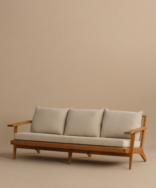 The Outdoor Vista Sofa is a modern teak outdoor sofa with three light gray Tempotest fabric cushions and matching pillows, shown against a plain beige background.