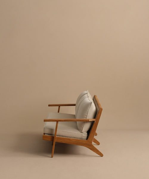 The Outdoor Vista Sofa, featuring light beige Tempotest fabric cushions and a modern wooden frame, is displayed in profile against a plain beige background, highlighting its minimalist and elegant design.