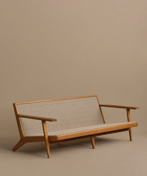 The Outdoor Vista Sofa features a minimalist teak frame with angled legs and arms, plus a woven beige seat and backrest. Shown on a plain beige background, its even comfier and more durable with Tempotest fabric cushions.