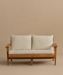 The Outdoor Vista Sofa, with a wooden frame, angled arms and legs, and off-white Tempotest fabric cushions, is displayed against a plain beige background.