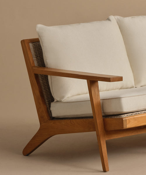 A close-up of the Outdoor Vista Sofa features light Tempotest fabric cushions, a beige backdrop, and highlights the armrest, angled legs, and textured seat details.