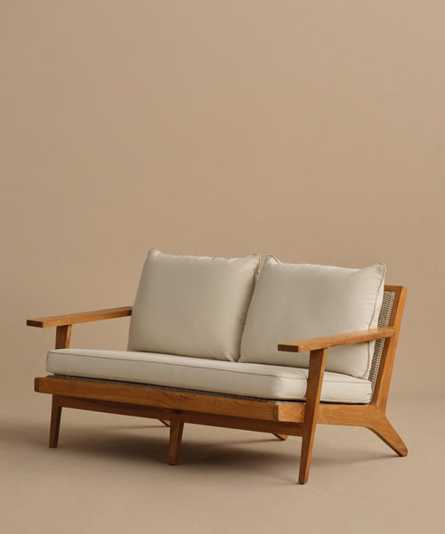 The Outdoor Vista Sofa features a wooden frame, angled legs, light Tempotest fabric cushions, and woven cane accents on the sides, displayed against a plain beige background.