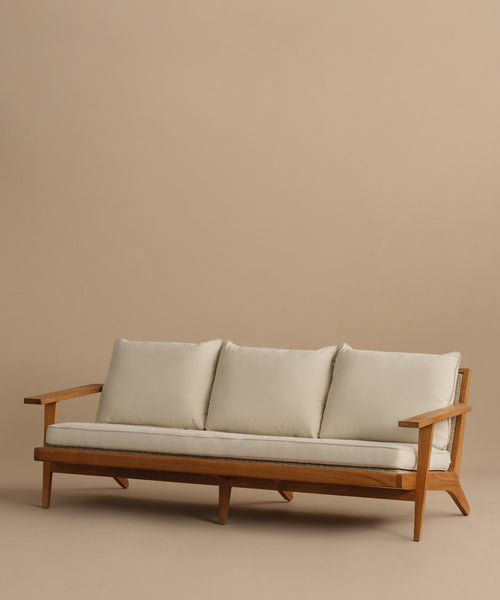 The Outdoor Vista Sofa is a mid-century modern teak piece with angled legs and armrests, including three off-white Tempotest fabric seat cushions and three matching back cushions, shown on a plain beige background.
