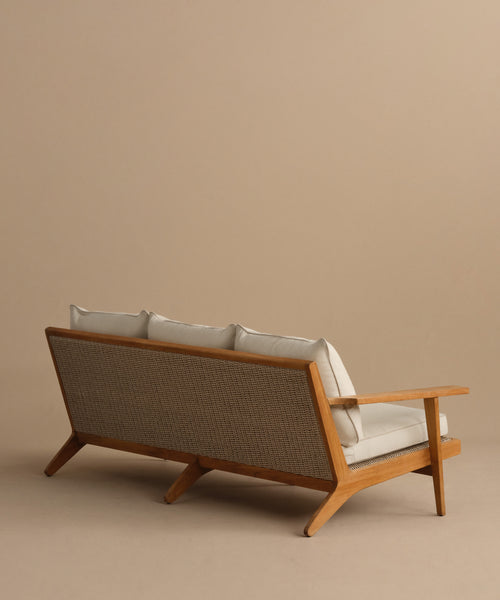 The Outdoor Vista Sofa features a mid-century modern design with light beige Tempotest cushions and a woven cane backrest, displayed against a neutral beige background.