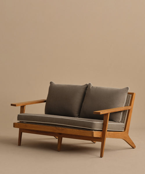 The Outdoor Vista Sofa features modern teak with angled legs, wide armrests, and two gray cushions for seat and back—ideal ECOLENE furniture for any contemporary space against a plain beige background.