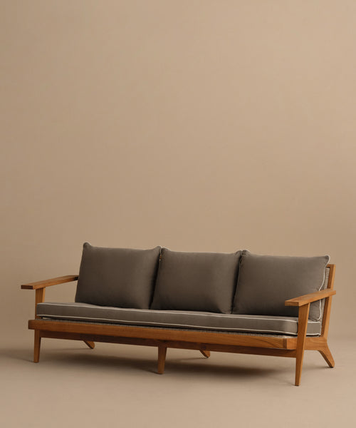 The Outdoor Vista Sofa features a teak wooden frame with angled legs and armrests, plus three gray seat and back cushions. It is shown against a plain beige background.