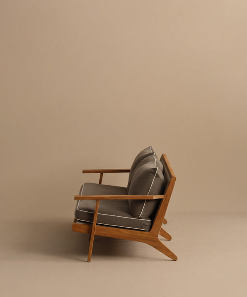 A modern wooden armchair with angled legs and gray cushions, set against a beige background—perfectly complementing the Outdoor Vista Sofa or other ECOLENE furniture in any stylish space.