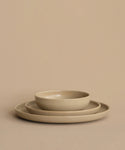 Three beige ceramic dishes are stacked against a matching background. The set includes a large plate, a smaller plate, and the Pacific Breakfast Bowl—a versatile and stylish stoneware bowl—arranged perfectly on top.