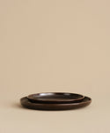 Two nested Pacific Salad Plates in dark brown from the Pacific collection rest on a beige surface against a plain beige background.