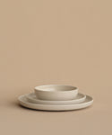 Three beige ceramic dishes, including a Pacific Salad Plate, are stacked on a neutral beige surface with a matching background; the smallest bowl sits atop two flat plates.
