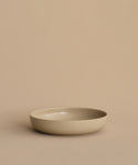 The Pacific Soup Bowl is a plain, shallow beige stoneware piece displayed on a matching beige surface with a neutral beige background.