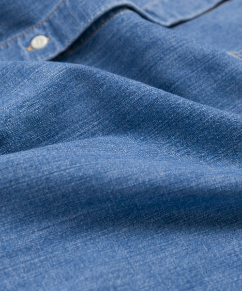 Close-up view of textured blue summer-weight denim with visible stitching, button, and seam details from the Parker Oversized Shirt.