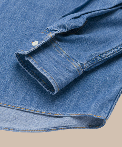 A close-up of the Parker Oversized Shirt shows its buttoned cuff, detailed stitching, and lightweight blue denim texture, set against a neutral background.