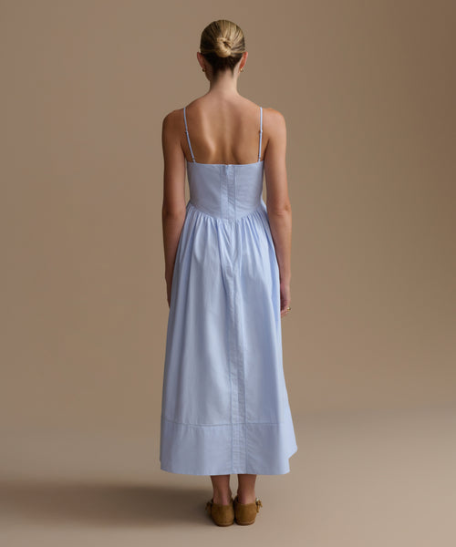 Woman wearing a light blue dress with thin straps on a beige background