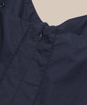 Close-up of the Peninsula Dress in navy Italian washed poplin, featuring a small black back zipper, visible stitching, and shown against a beige background.