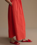 Woman wearing a long red dress and matching red sandals on a beige background