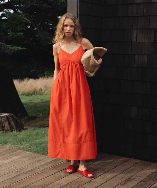 Woman in an red dress holding a woven raffia handbag on a wooden deck.