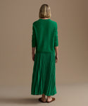 Woman wearing a green cashmere sweater and a green pleated skirt standing against a beige background