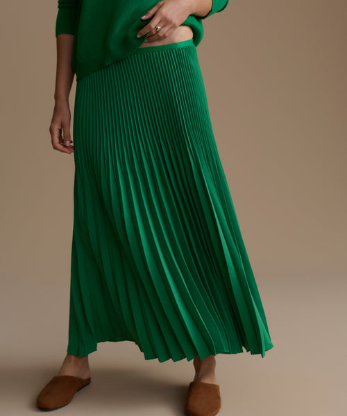 Green pleated skirt worn by a person on a beige background