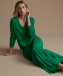 Woman wearing a green cashmere sweater and a green skirt sitting on a beige background