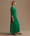 Woman wearing a green pleated skirt and green cashmere sweater against a beige background