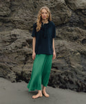 Person wearing a navy top and green skirt standing on a rocky beach.