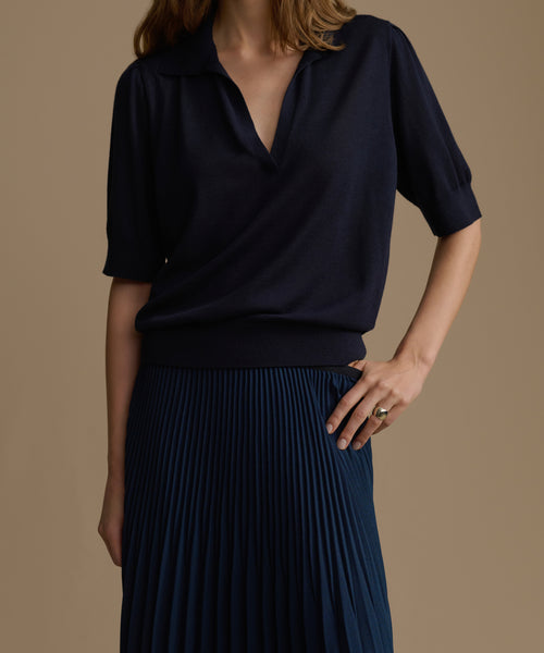 Person wearing a navy blue top and navy pleated skirt on a beige background