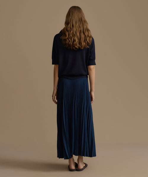 Person wearing a navy top and pleated navy skirt on a beige background