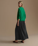 Woman wearing a green sweater and slate pleated skirt on a beige background