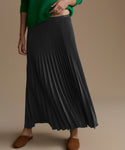 Person wearing a green sweater and slate pleated skirt on a beige background