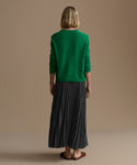 Person wearing a green sweater and slate pleated skirt on a beige background
