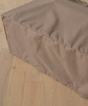 A close-up of the Outdoor Vista Coffee Table Cover, a light brown, rectangular fabric cover resembling an outdoor furniture accessory, placed on a light wood floor.