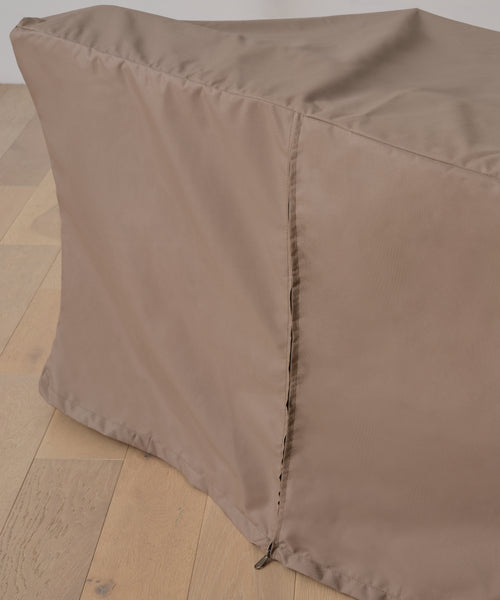 A close-up of the Outdoor Vista Sofa Cover in brown, draped over a rectangular object on a light wood floor. The cover has a visible seam and zipper along one edge, providing waterproof protection for patio furniture.