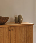 Three ceramic vases on a wooden cabinet against a plain wall.