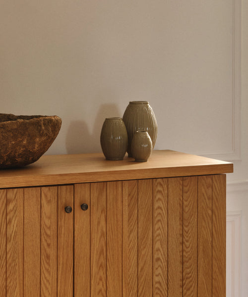 Three ceramic vases on a wooden cabinet against a plain wall.