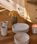 A dining table with a vase with flowers, dinnerware and a candle.