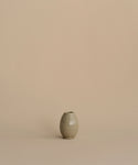 A small ribbed ceramic vase in a muted sage green-gray color, centered against a solid warm beige background.