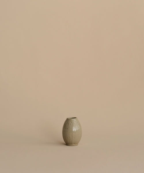 A small ribbed ceramic vase in a muted sage green-gray color, centered against a solid warm beige background.