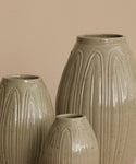 Three ribbed ceramic vases in a speckled light beige glaze, arranged against a solid warm beige background.