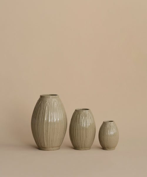 Three ribbed ceramic vases in a light beige-gray glaze, arranged by size against a solid warm beige background.