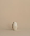 A small cream-colored ceramic vase with a ribbed, lotus-like texture, centered against a solid, warm beige background.