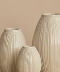 Three ribbed ceramic vases in a warm cream-beige color, arranged against a solid beige background.
