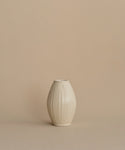 A small cream-colored ceramic vase with a textured vertical ribbed pattern, centered against a solid beige background.