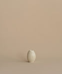 A small cream-colored ceramic vase with a ribbed, lotus-like texture, centered against a solid, warm beige background.