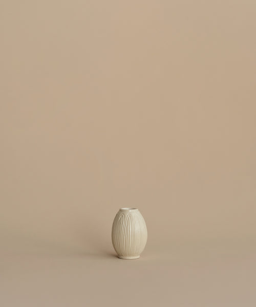 A small cream-colored ceramic vase with a ribbed, lotus-like texture, centered against a solid, warm beige background.