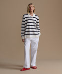 Woman wearing a navy stripe post pullover with white pants on a beige background